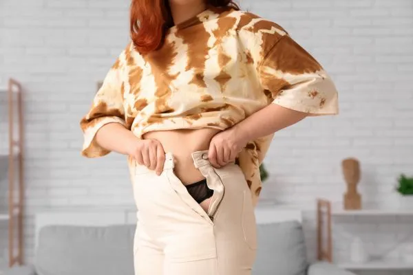 Image of woman trying to do her trousers up after pregnancy weight gain Scotland